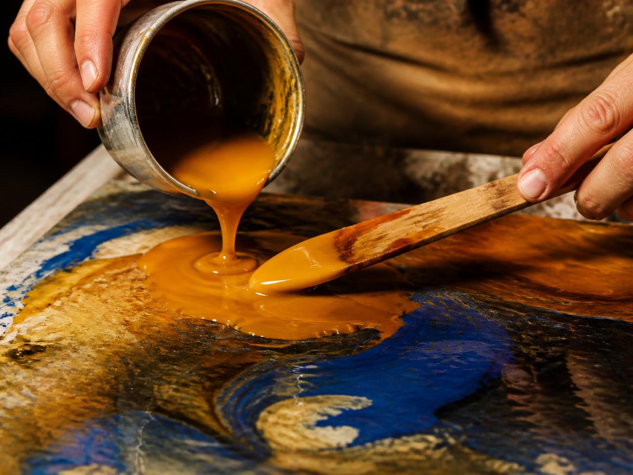 Hands pouring molten encaustic paint from a silver tin